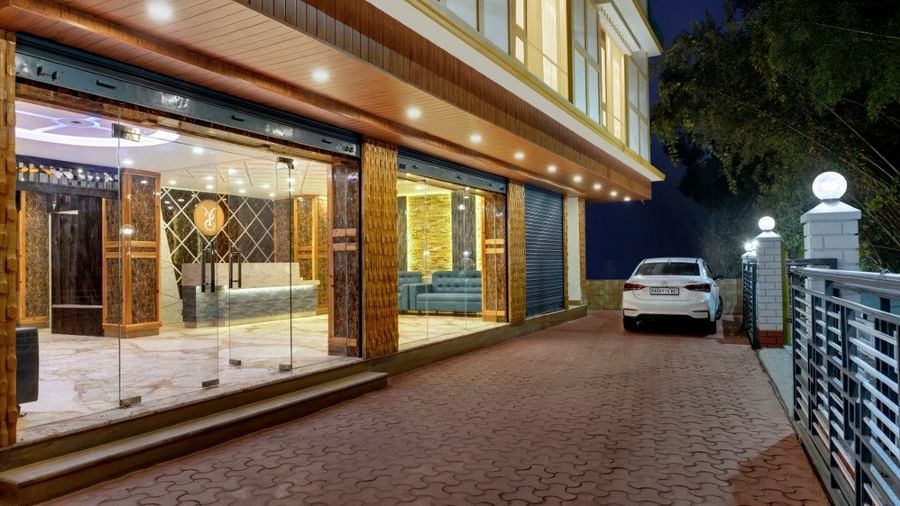 An evening facde view of Yashshree Sikkhim Blossom in Gangtok showcasing the well-lit entrance, glass-front lobby, and driveway with a parked car.  