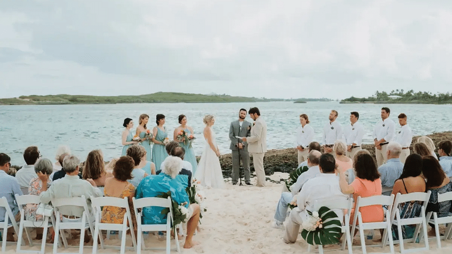Beach wedding ceremony with guests seated on white chairs, facing the couple under an open sky with the sea behind | Abaco Inn