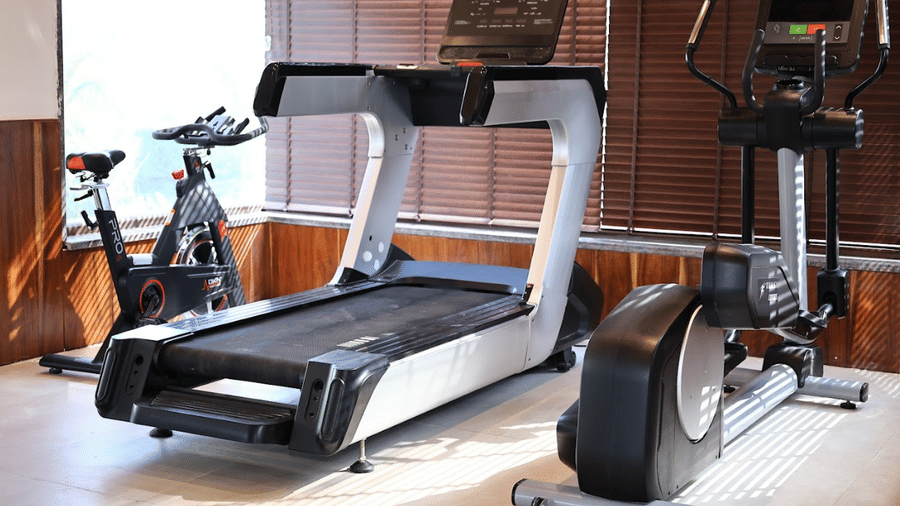 Modern gym interior featuring a treadmill, elliptical trainer, and stationary bike near sunlit windows.