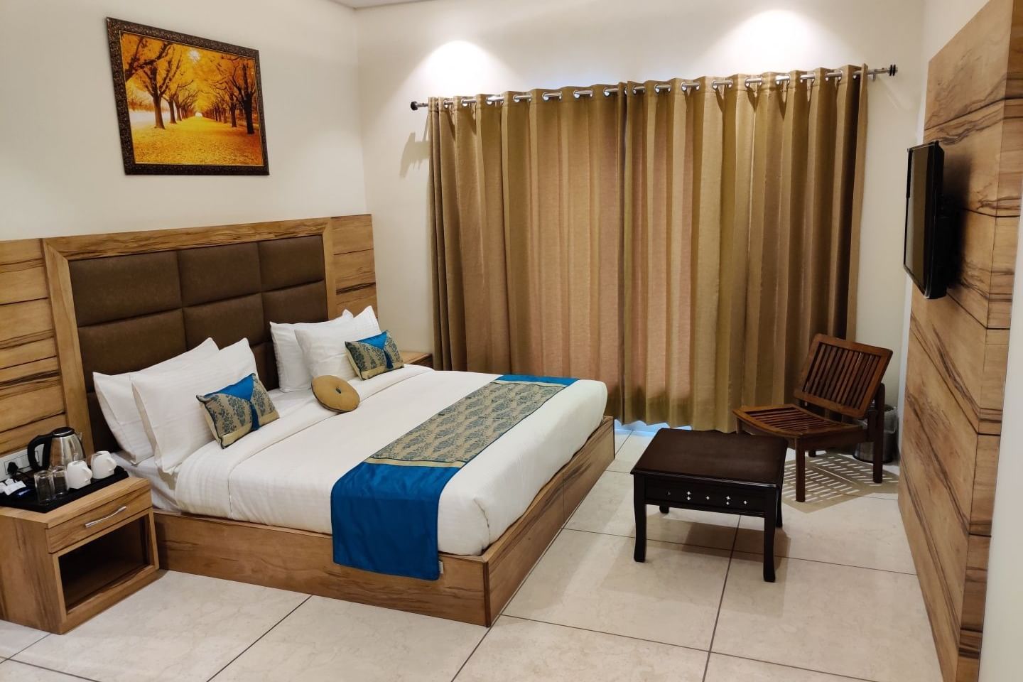 A bedroom with a large bed, a comfortable chair, and a flatscreen TV. The room is well-lit with natural and artificial light.