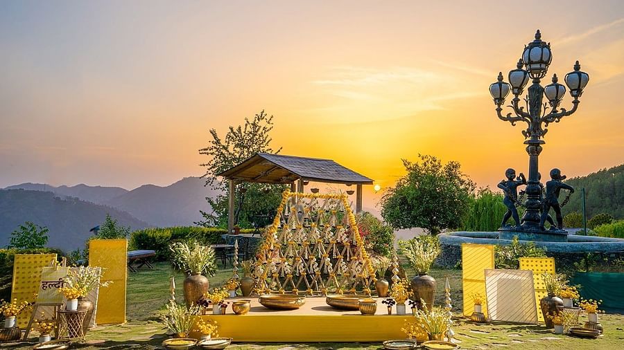 Traditional Haldi setup at The Manor Sports & Wellness Hotel featuring yellow decor, brass vessels and a floral swing with mountains and sunset skies in the backdrop.