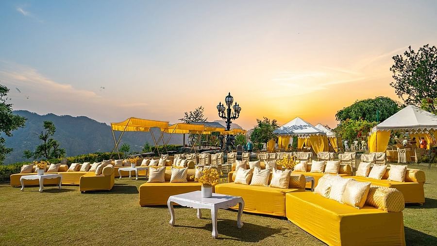  Outdoor seating with yellow sofas and white cushions arranged for a wedding function at The Manor Sports & Wellness Hotel, under a golden sky and canopies.