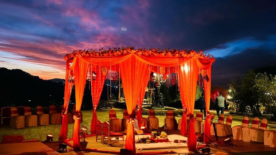  Traditional mandap draped in red fabric under a twilight sky at The Manor Sports & Wellness Hotel, ready for a wedding ceremony with scenic hill views.