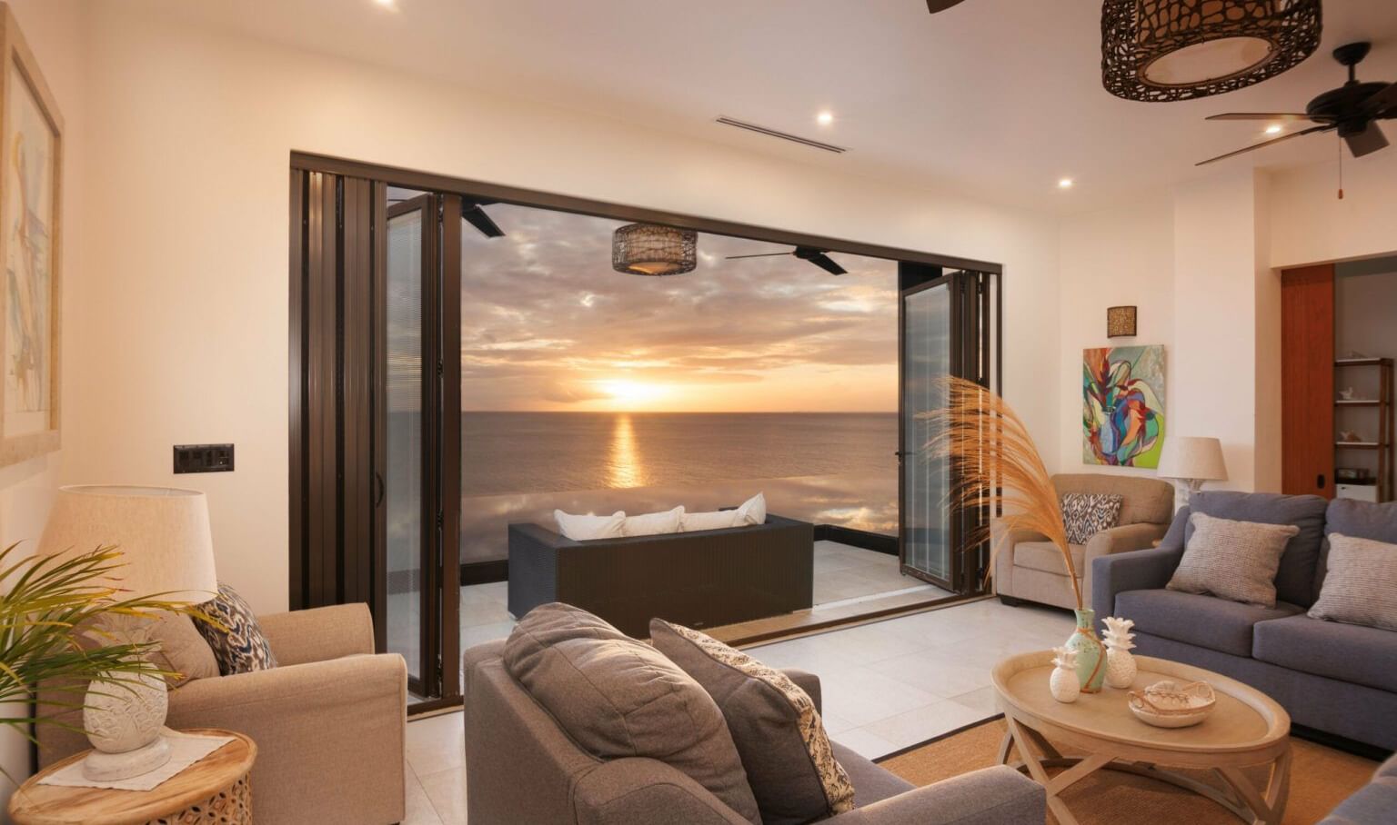 A modern living room with large sliding glass doors opening to an outdoor patio with a view of the sunset.
