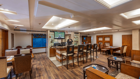 a restaurant at Libra Lords Inn Jaipur with a bar counter with high bar chairs, wall-mounted TV, and various seating arrangements 