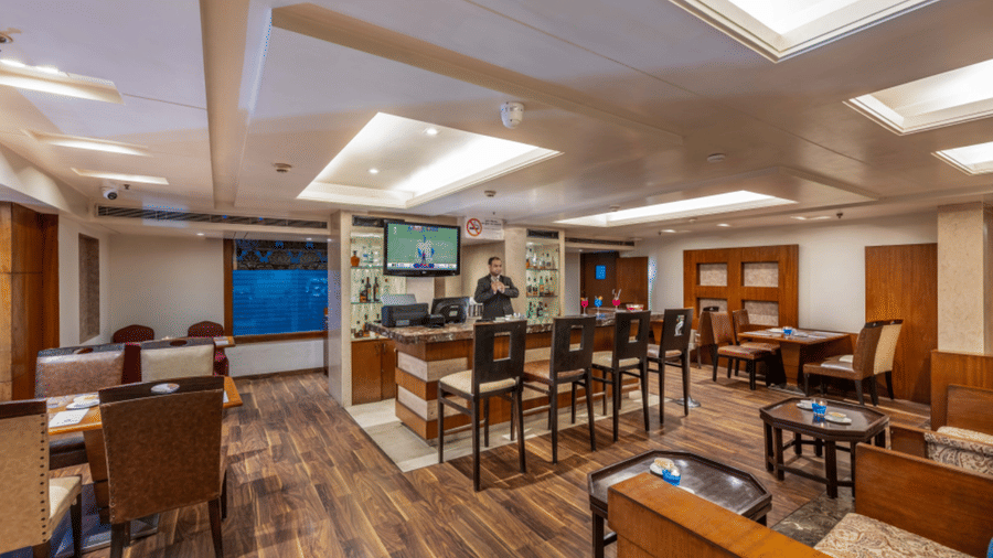 a restaurant at Libra Lords Inn Jaipur with a bar counter with high bar chairs, wall-mounted TV, and various seating arrangements 