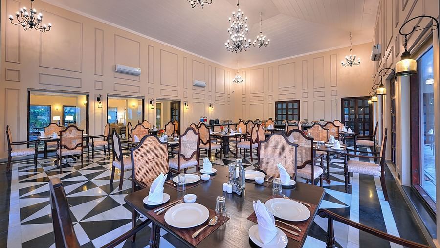 Elegant dining hall with chandeliers, classic decor, and neatly arranged tables set with fine dining essentials. Large windows and warm lighting create an inviting ambience - Singhvilas, Ranthambore