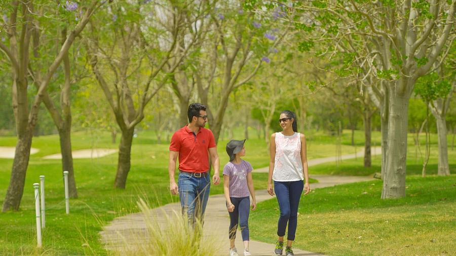 A family of three walking on a pathway next to manicured garden - Karma Lakelands.