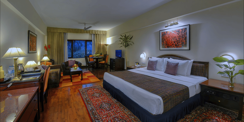 A Junior Suite at The Clarks Varanasi featuring a neatly-made bed, a patterned carpet, wooden furniture and a seating area.