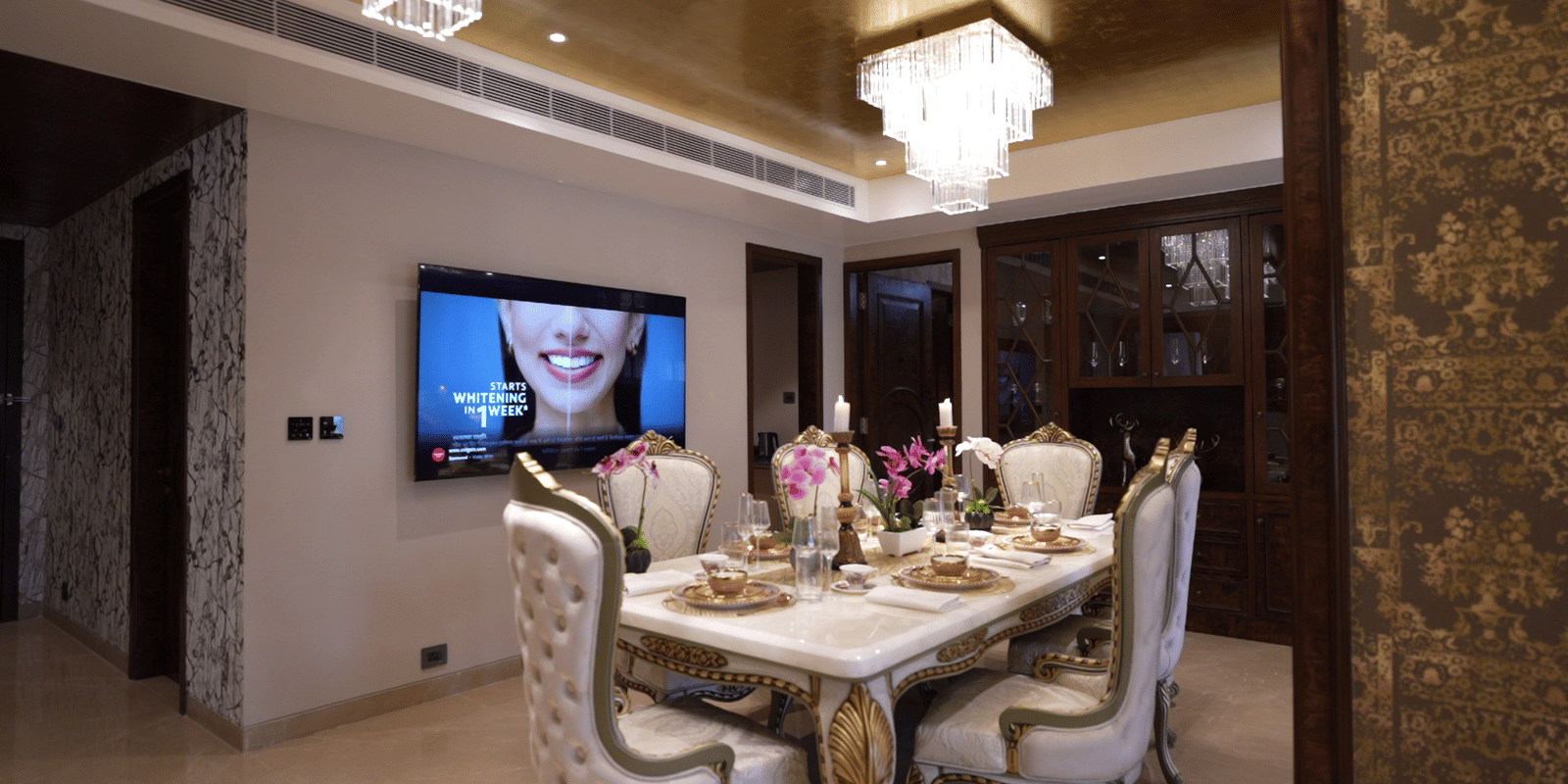 Elegant dining room with a set table, ornate chairs, high-gloss ceiling, and a television mounted on the wall.