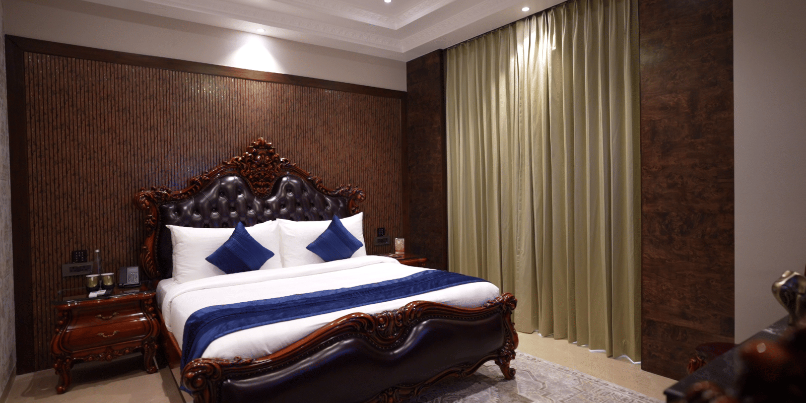 Luxury master bedroom showcasing a dark wooden bed frame with royal blue bedding and textured wall panelling.