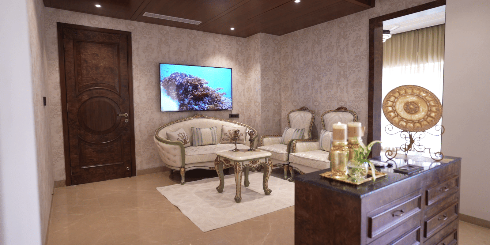 Luxurious contemporary living space with ornate carved wooden door, curved sofa, flat-screen TV, and decorative dresser.