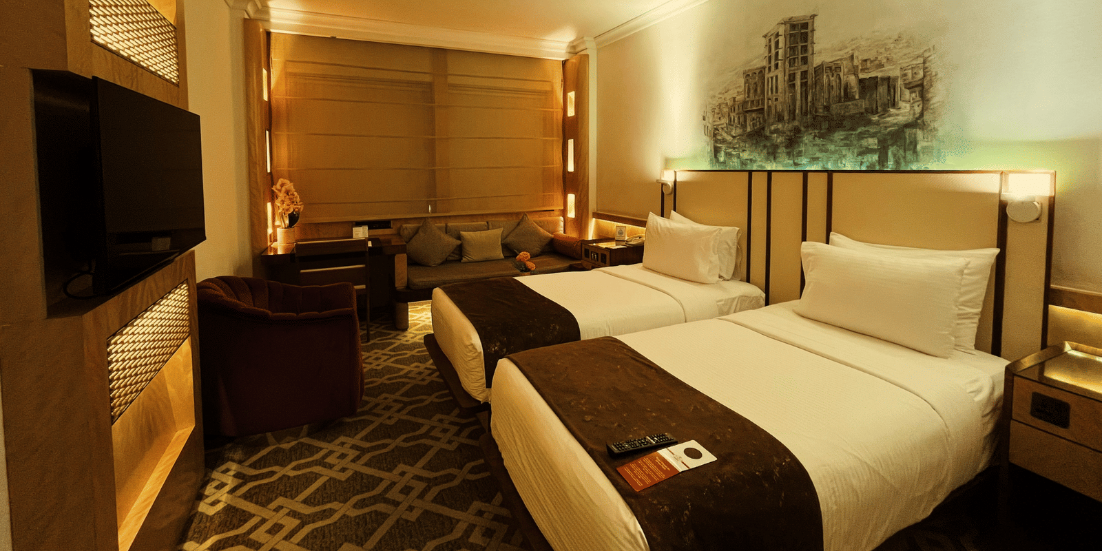 Wide shot of two twin beds, a television screen, and an armchair in a room at Marco Polo Hotel.