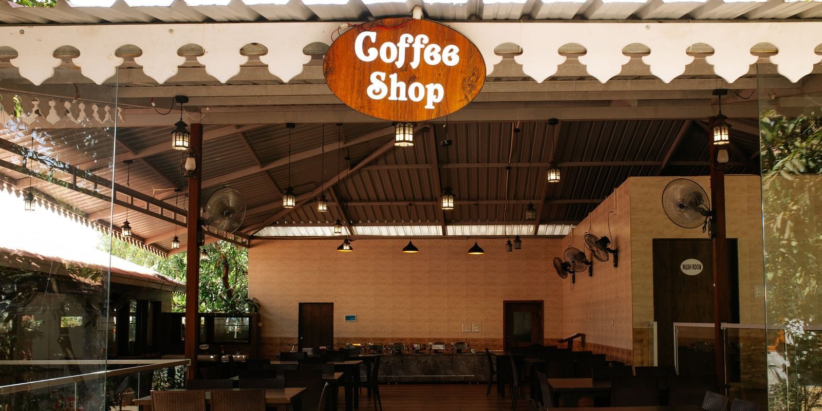 A view of the dark, empty Coffee Shop area with black tables and a glass railing, at Daksh Resort & Amusement Park, Sasan Gir.