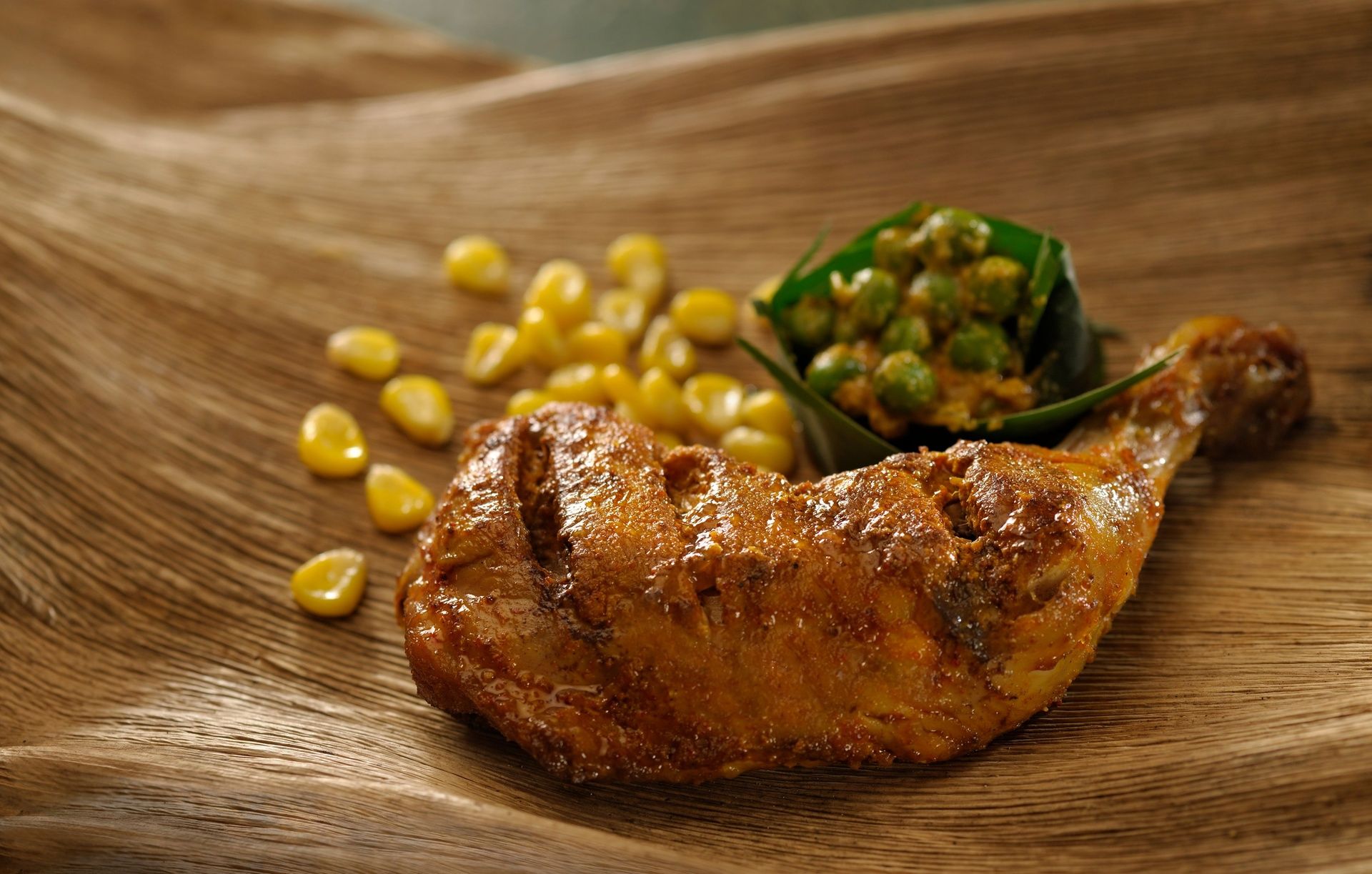 Roasted chicken leg with corn and peas on a plate.