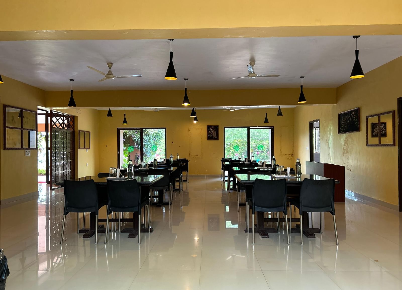 Restaurant interior with tables, chairs, indoor tree section, and yellow walls at Paradise Wild Hills Resort, Kollur.