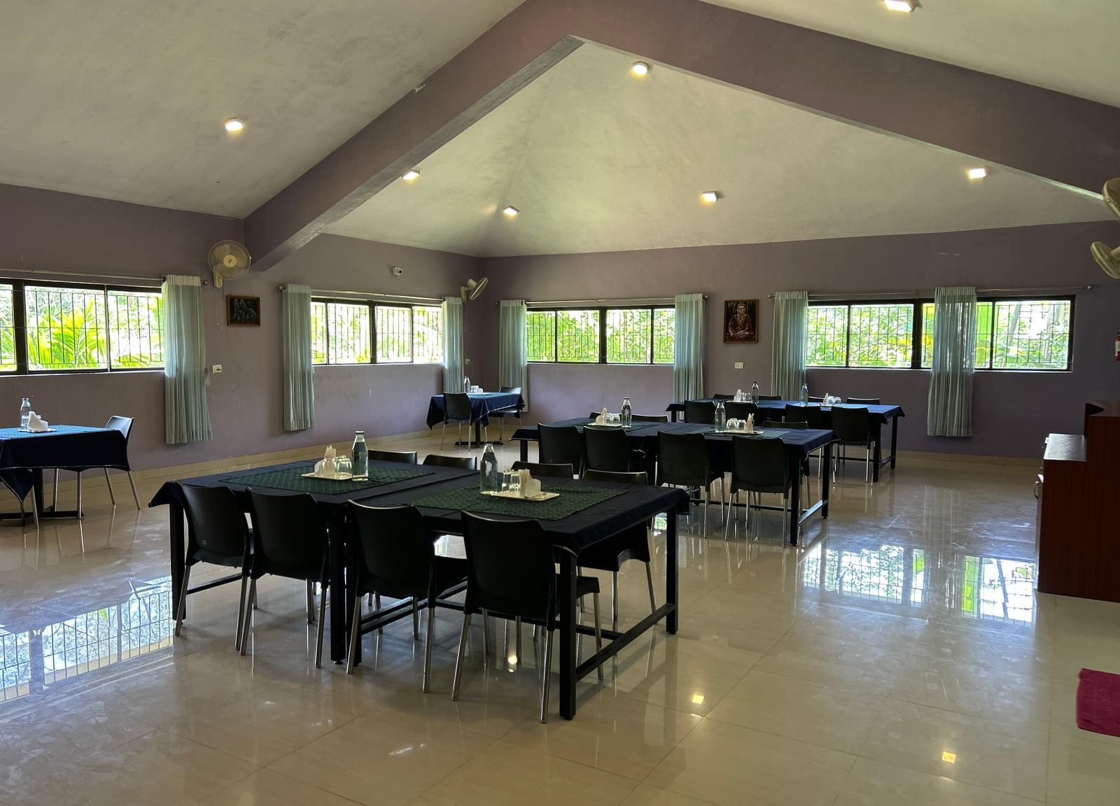 Spacious dining hall with black tables, chairs, tiled floor, and large windows at Paradise Wild Hills Resort, Kollur.