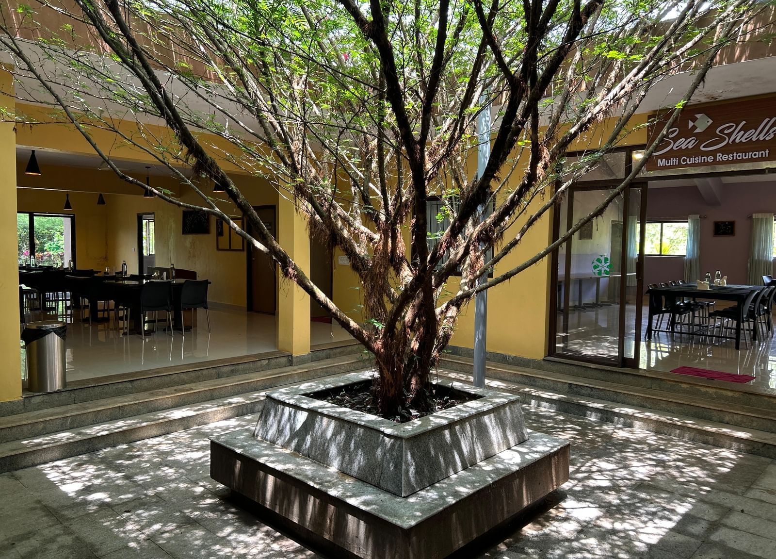 Courtyard area with a tree surrounded by seating and open dining sections at Paradise Wild Hills Resort, Kollur.