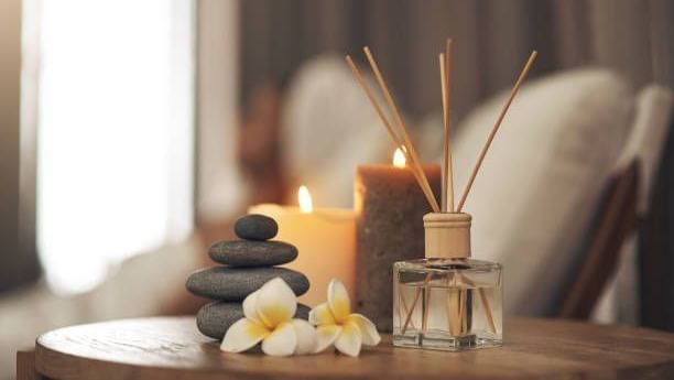 Relaxing spa-like scene with candles, diffuser, stones, and flowers.