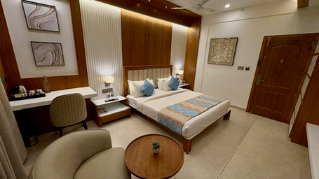 The deluxe room seating and work area with a lounge chair, round side table, writing desk, and framed artwork near the bed at Dwarkadhish Lords Eco Inn.