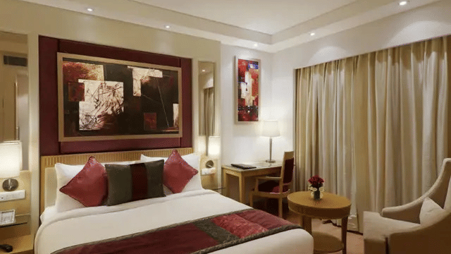A room at Eastlynn Collections Huda City Centre, Gurugram, features a large bed, dark artwork, and a small desk.