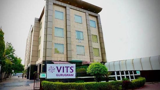 A low-angle exterior shot of a multi-storey building with a sign that reads VITS GURUGRAM, surrounded by greenery