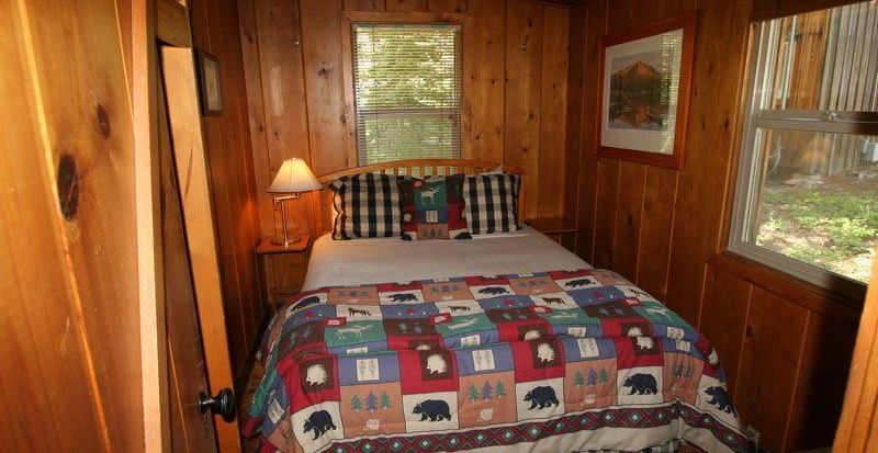 A snug cabin bedroom with  a bed and a colorful patchwork quilt. - Kit Carson Lodge & Restaurant