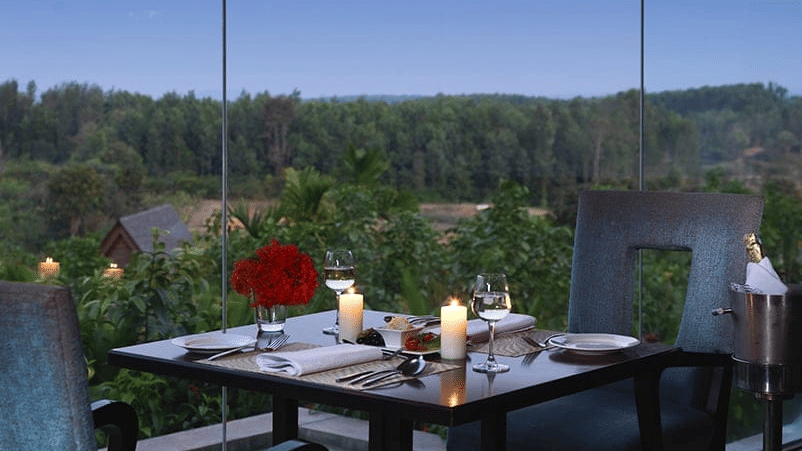 A table for 2 set against a scenic view of the nature at Odyssey Restaurant at The Serai Chikmagalur