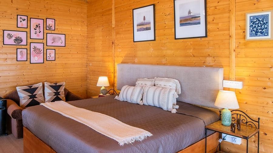 An image of a bedroom with double size bed frames hanging on the all, bedside table on either side, and a light hanging from the ceiling - Avalon Cottages, Kanatal