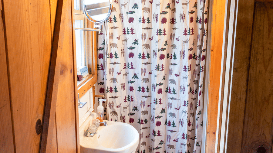A compact bathroom at Kit Carson Lodge featuring a shower area with a patterned curtain, a small sink, and wooden paneling throughout