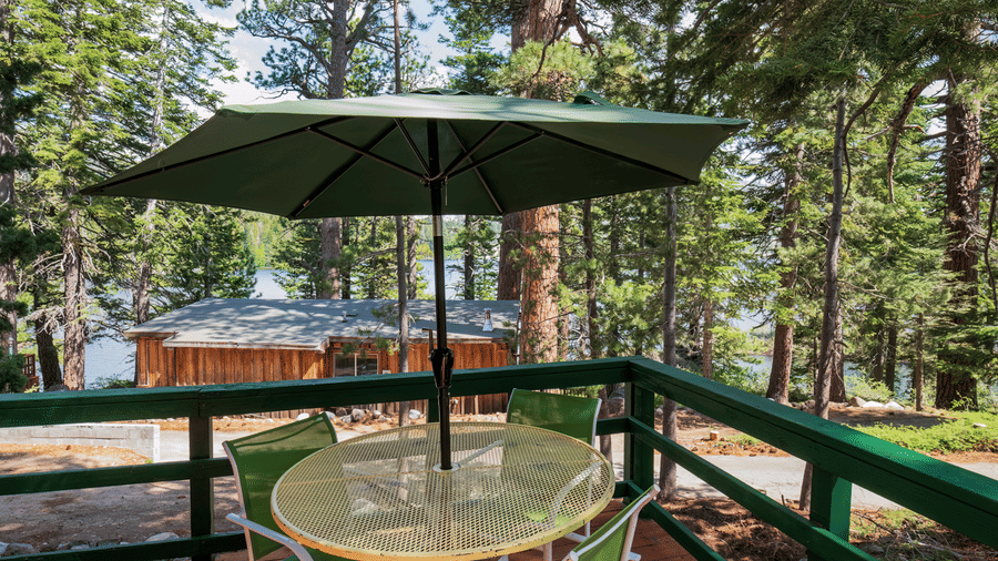 A deck at Kit Carson Lodge with a patio table, chairs, and an umbrella overlooking tall pine trees