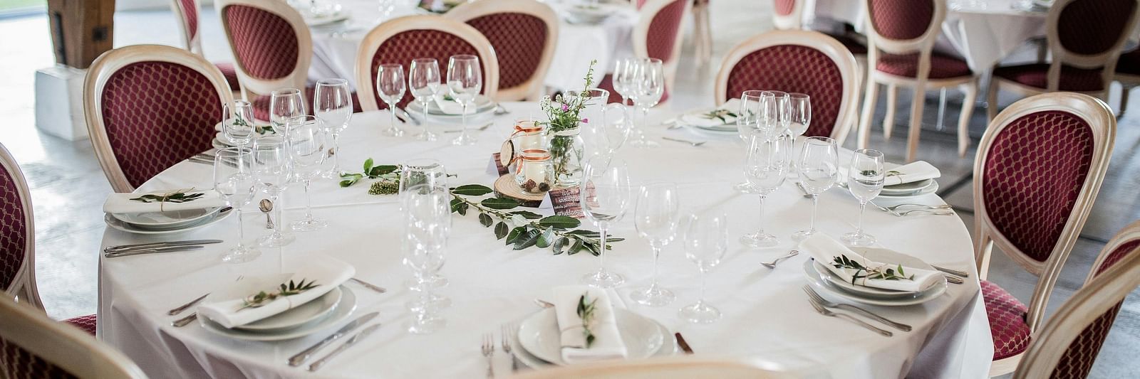 Tables set for a formal event with elegant white tablecloths and red chairs.