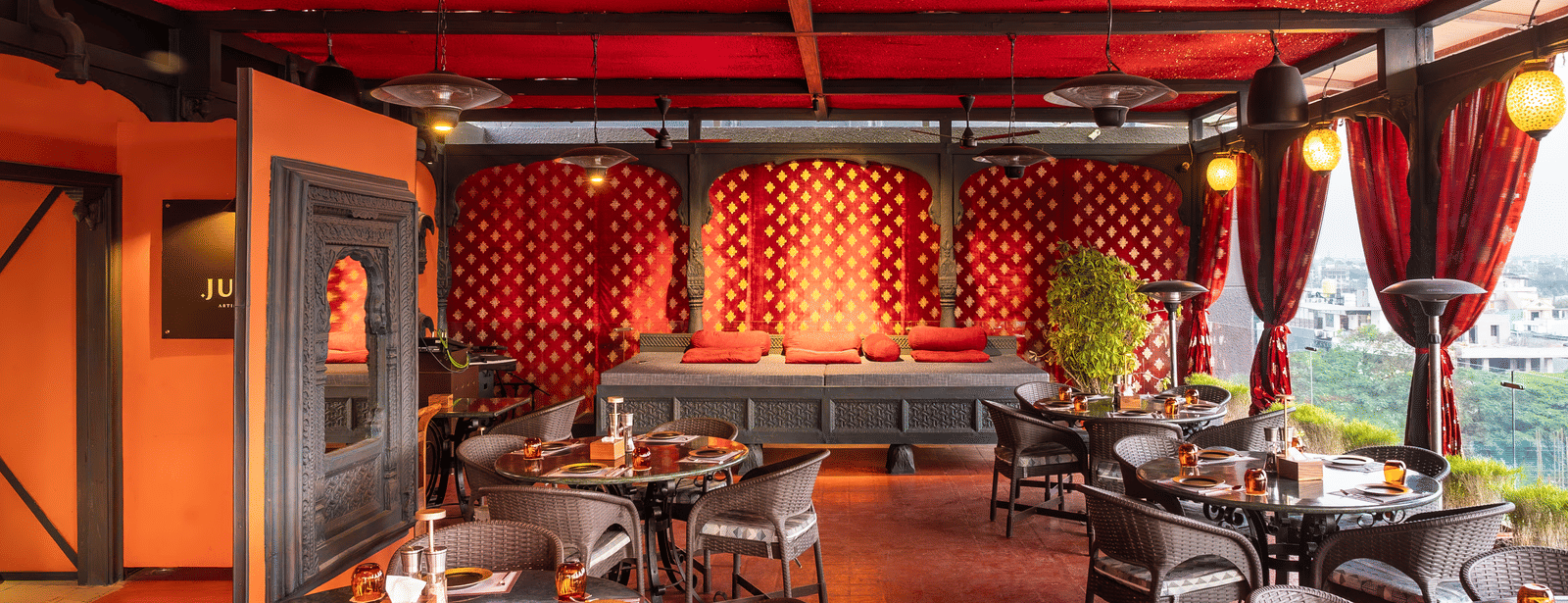 A restaurant interior with red ceiling, patterned walls, and dining tables with chairs at Infiniti Hotel, Indore.