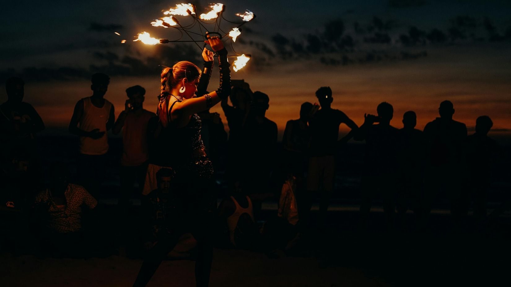 Fire performer entertaining a crowd under a night sky with orange hues.