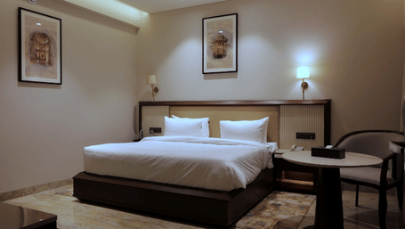 Deluxe Room at Raj Leela Heritage Resort by Estherea, Ranakpur featuring a king size bed, 2 wall paintings, bedside lamps, and table with 2 chairs.