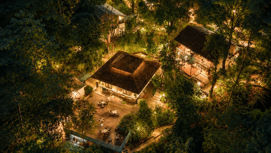 Aerial twilight view of the warmly-lit resort structures nestled within a dense forest at Neemrana's Glasshouse on The Ganges - 21st Century, Rishikesh.