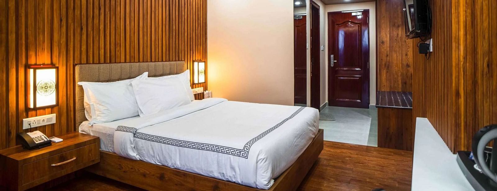 A cozy bedroom at Mansha Palace features wooden paneling, a comfortable bed, and a ceiling fan.