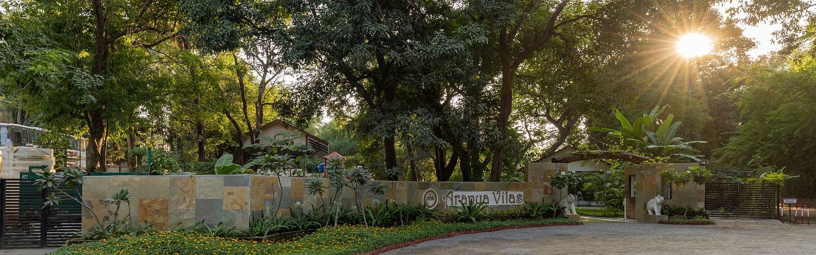 exterior image of aranya vilas featuring the resort logo on the wall on a bright morning with a bright sun in the background