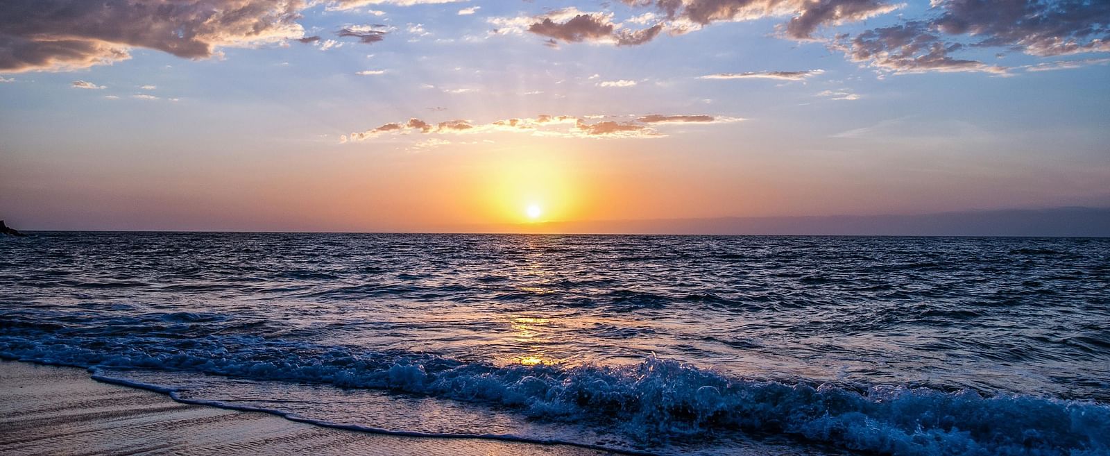 A beachfront view of the sunrise with clouds scattered across the sky.
