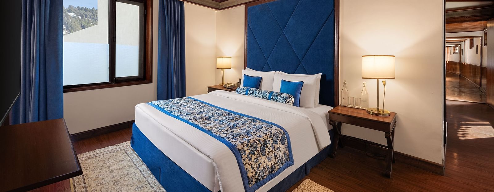 An image of a  cozy room in the naini retreat, nainital, with a king-size bed, wooden furniture, and a window. The room also features a ceiling fan.