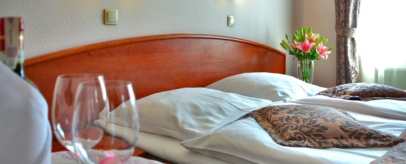 A well-prepared hotel room with a made bed, wine glasses, and soft lighting.