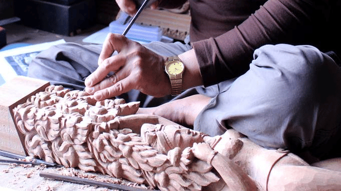 A skilled local artisan meticulously chiseling intricate patterns onto a wooden block in a traditional craft workshop in Bhaktapur, Nepal.