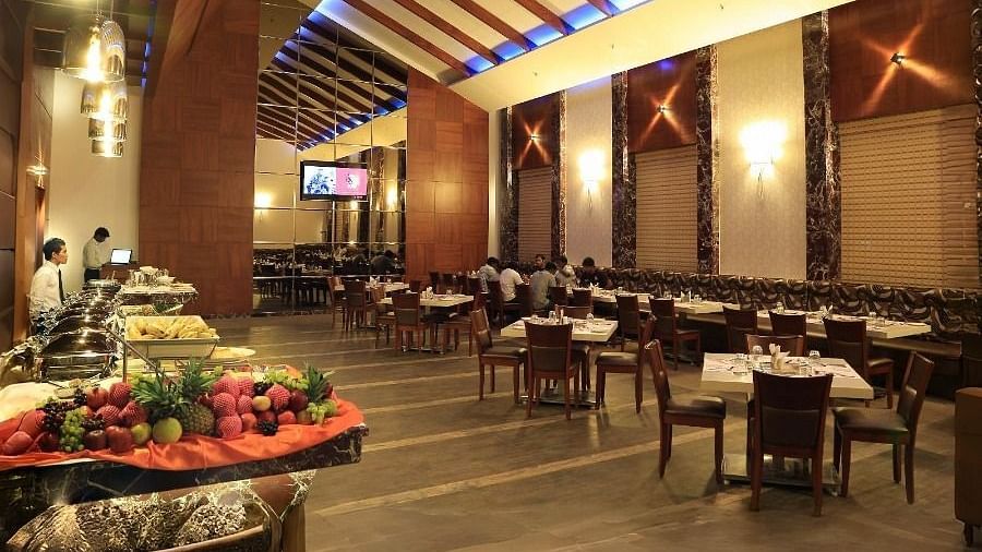 The interior of the Aroma restaurant in Dhanalakshmi Srinivasan Hotels, Perambalur, showing a buffet spread, dining tables, and chairs. The restaurant features wooden ceiling beams and tiled flooring.