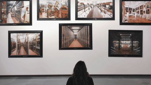 a girl sitting on a bench looking at the paintings hung inside a museum