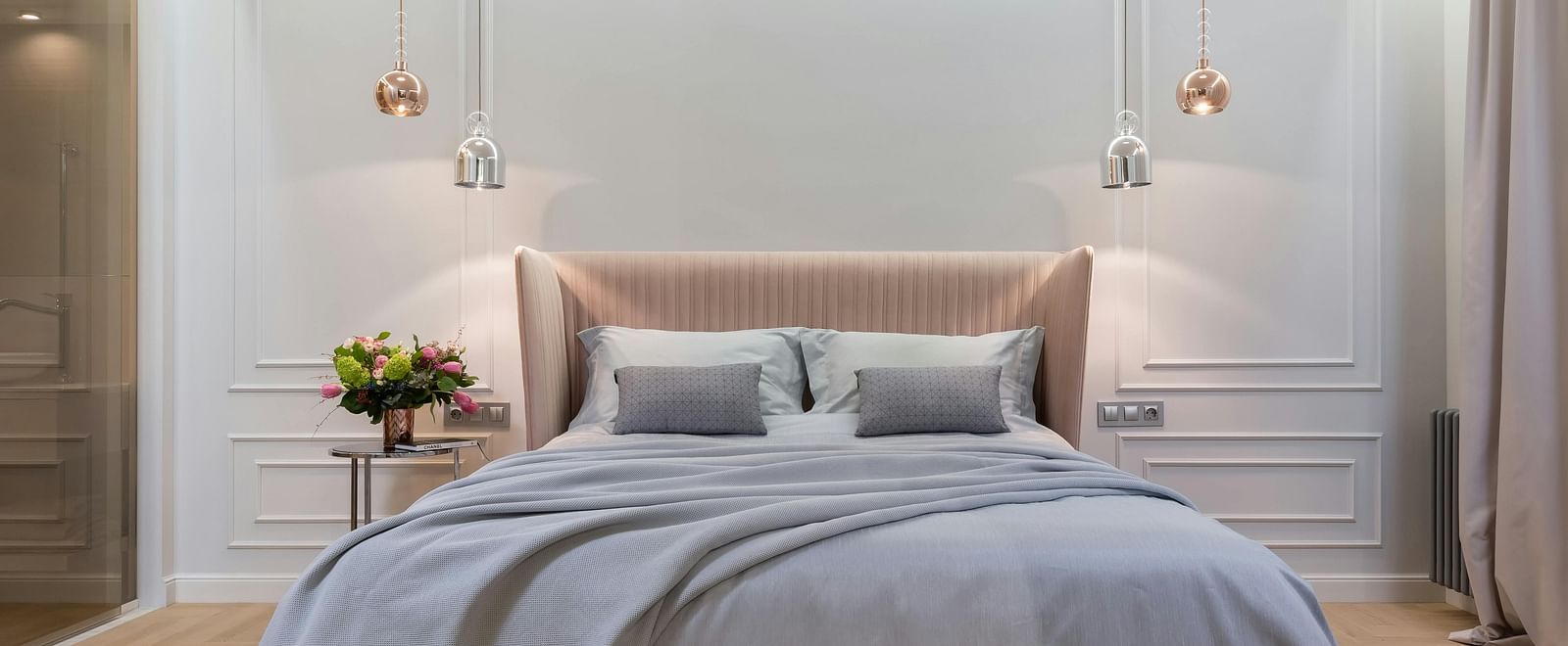 A modern bedroom is shown with soft lighting, a grey duvet, and a tufted bench.