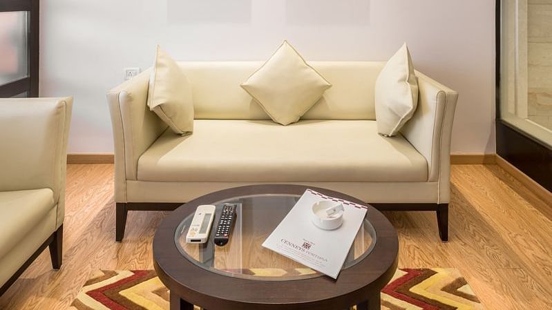 A cosy hotel suite corner with a sofa, coffee table and unique lamp hanging from the ceiling - TGI Grand Fortuna, Hosur