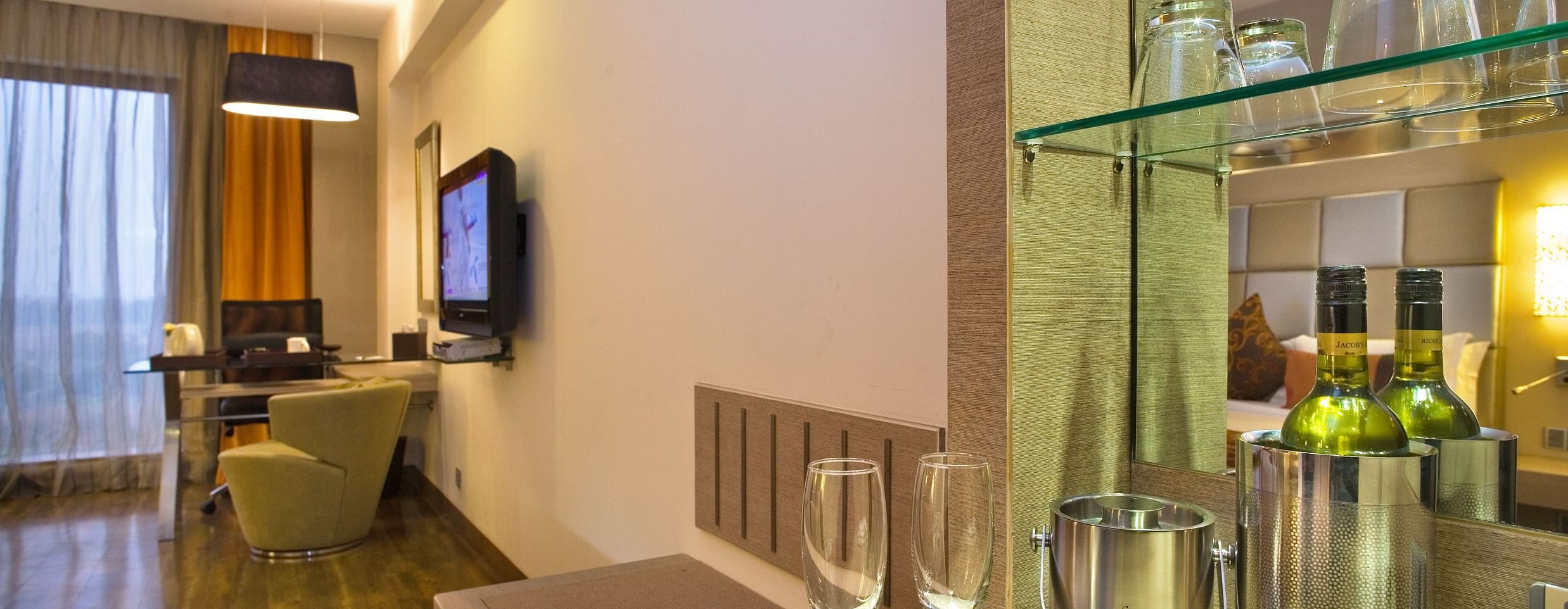 An interior view of a hotel room featuring a bar setup with glassware and bottles, a desk, and a chair- The Sonnet, Kolkata.