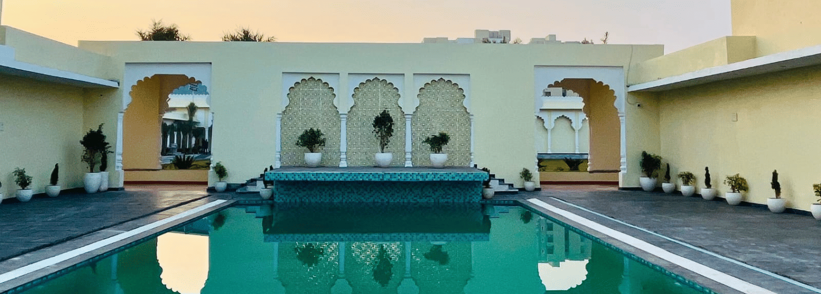 Outdoor swimming pool surrounded by arched buildings with seating areas at Beelwa Palace, Jaipur
