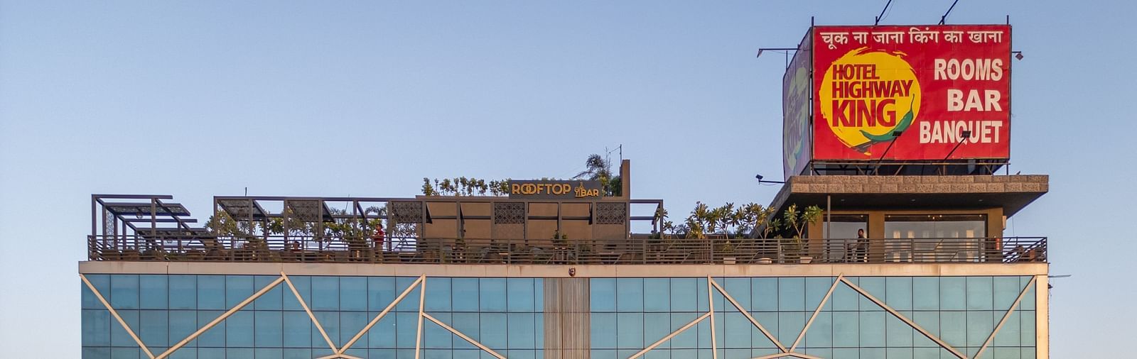 Exterior view of Hotel Highway King with glass facade and signage, surrounded by green trees.