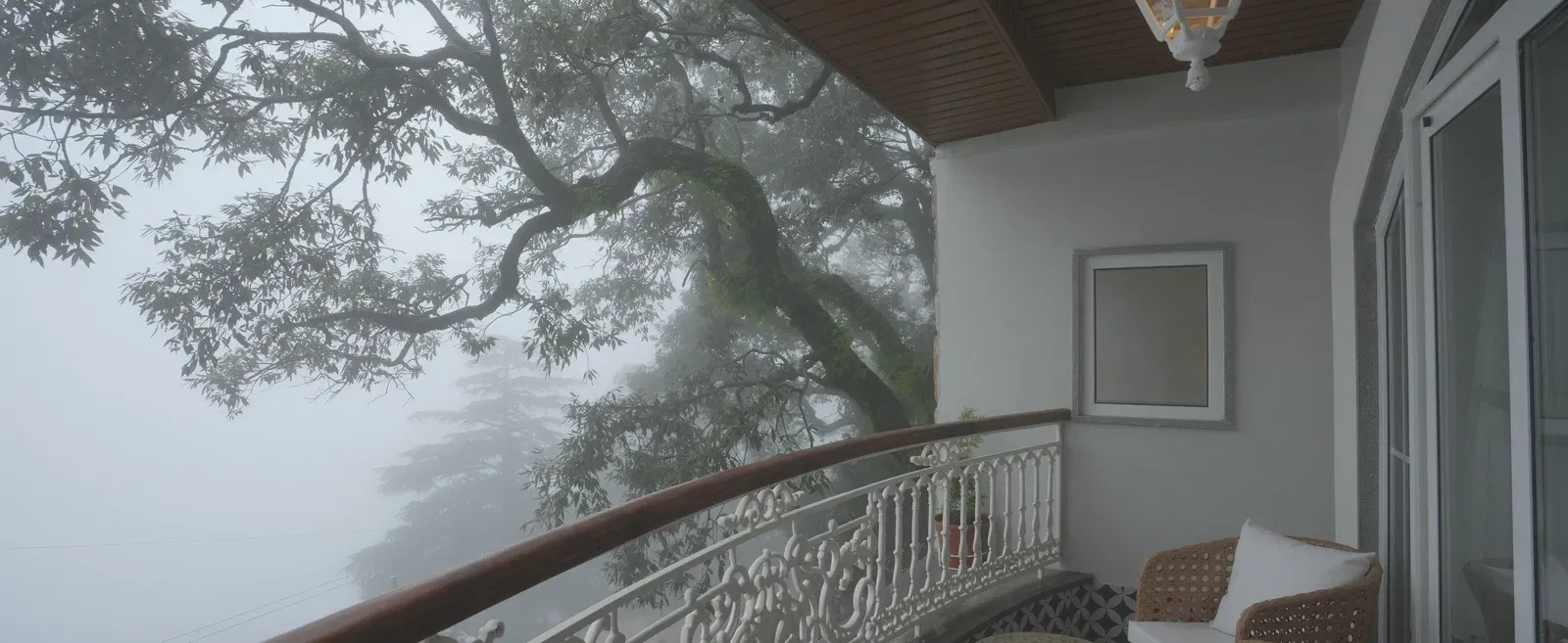 Balcony with rattan seating and misty views through forest trees - Mayfair Cafe & Suites, Dalhousie